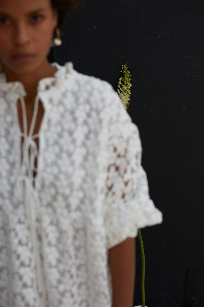 Junge Frau im Fotostudio mit weißem Kleid vor schwarzer Wand. Das Bild ist sehr ästhetisch und unscharf.