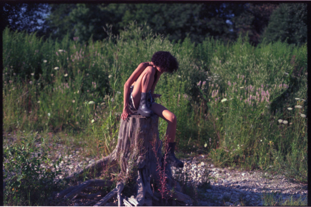 junge Frau sitzt auf einem Baumstumpf und versucht gerade aufzustehen.