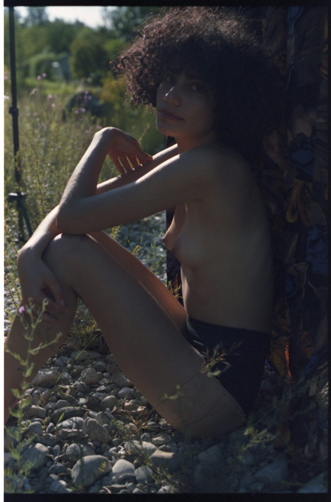 Junge Frau sitzt Barbusig vor einem Stoffhintergrund in der Natur. Sehr reduziert und intim.