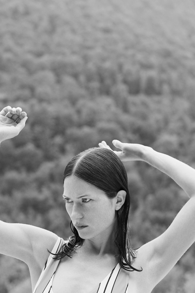 schwarz weiß foto, model im badeanzug mit armen in der luft, vor wald, angeschnitten