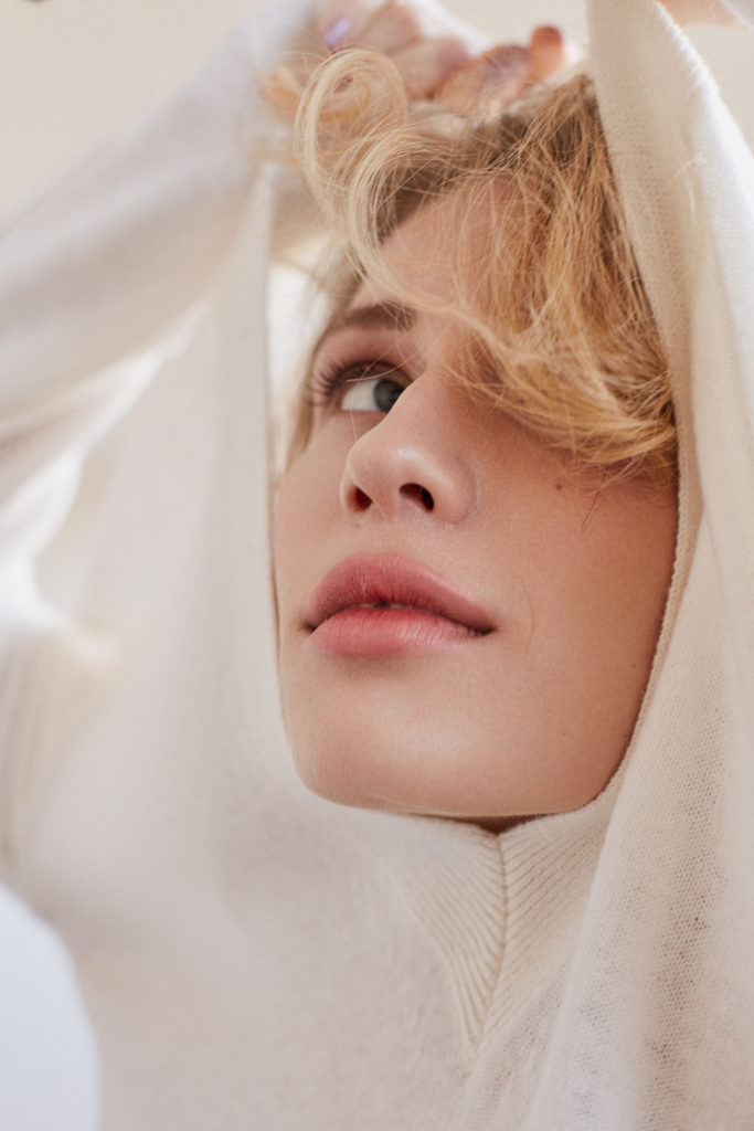 Ein Model zieht sich gerade den Pulli über den Kopf. Zu sehen ist nur noch das Gesicht im Ausschnitt. Sehr künstlerisch.