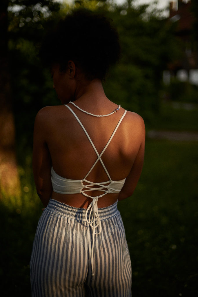 Ein stimmungsvolles Foto einer schwarzen Frau im späten Sonnenlicht mit einem Bikinitop und einer Leinenhose.