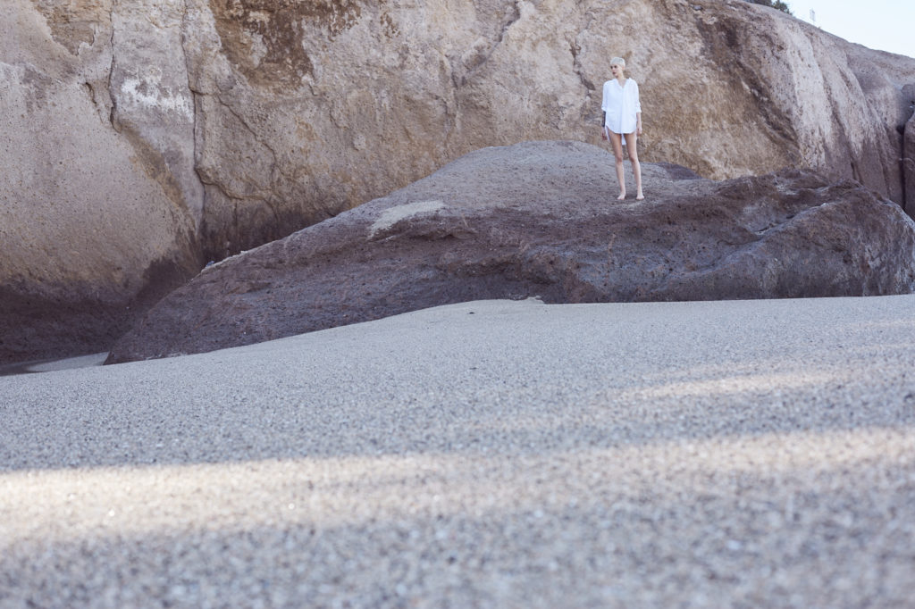model-steht-auf-felsen-in-der-ferne-in-weißer-bluse