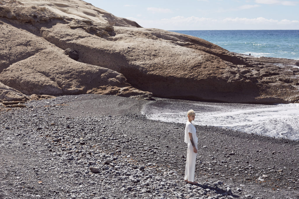 model-steht-an-strand-ganz-in-weiß-dunkler-kiesstrand