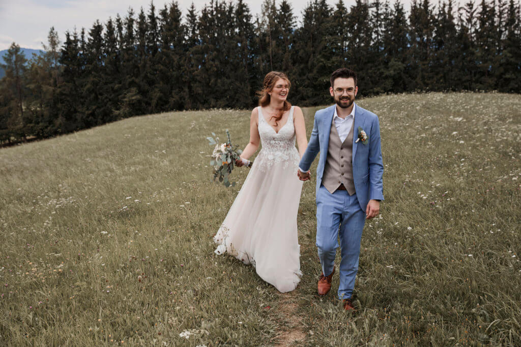 Brautpaar geht auf Wiese, er vorraus