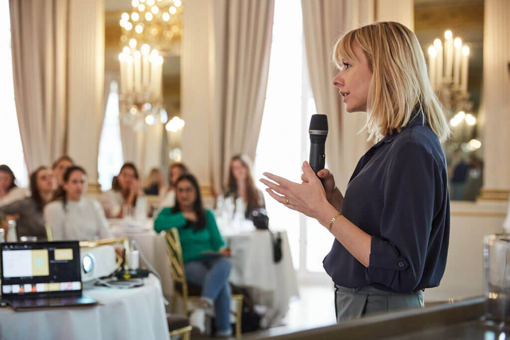 Magarethe Hoenisch bei einem Finanzevent mit Mikrofon in der Hand.