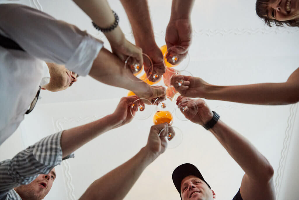 mehrere hände von unten mit getränken, die gemeinsam anstoßen.