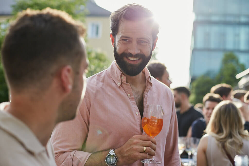 attraktiver junger mann mit bart und getränk in der hand lächelt anderen mann an.