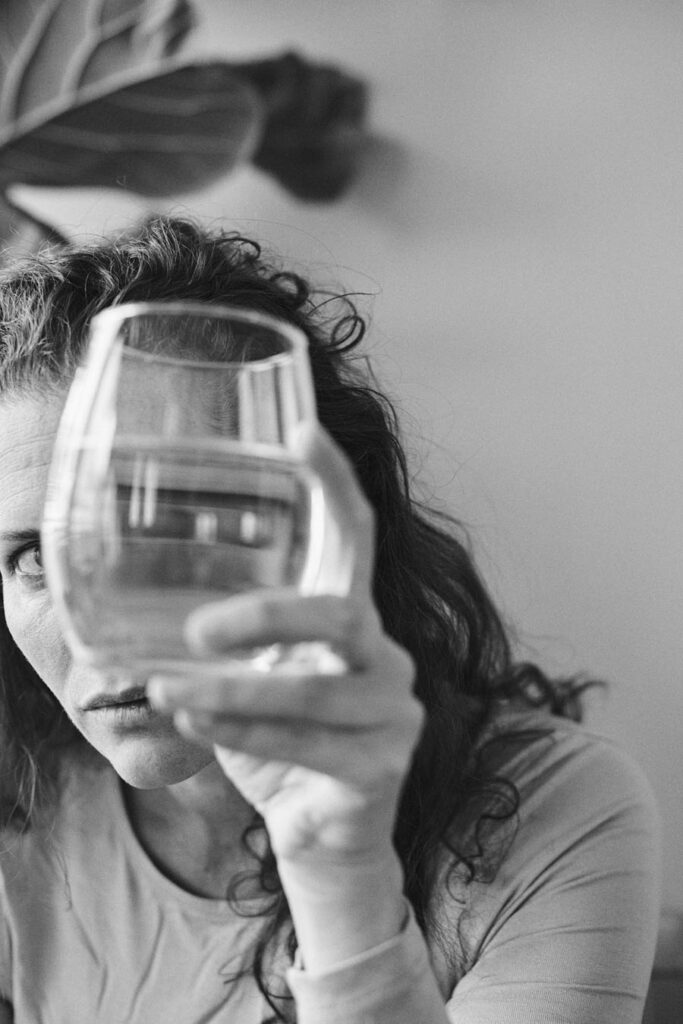 eine schwarz weiß fotografie von einer frau, die durch ein glas mit wasser schaut. minimalistisch und künsterlisch.