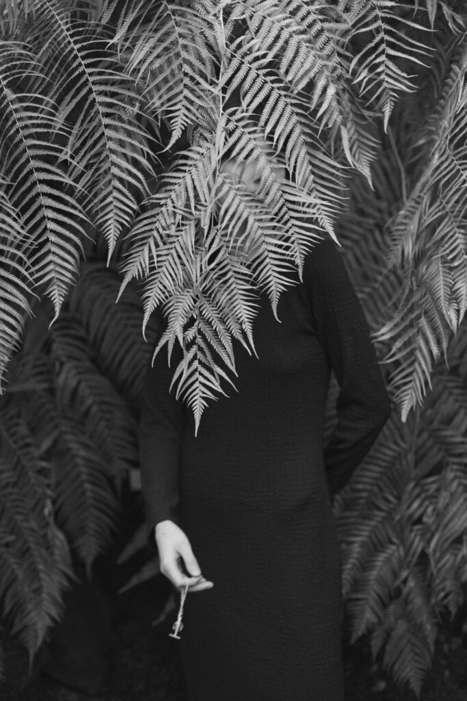 Sehr künstlerische schwarz weiß Fotografie eines weiblichen Models hinter einer Pflanze stehend.