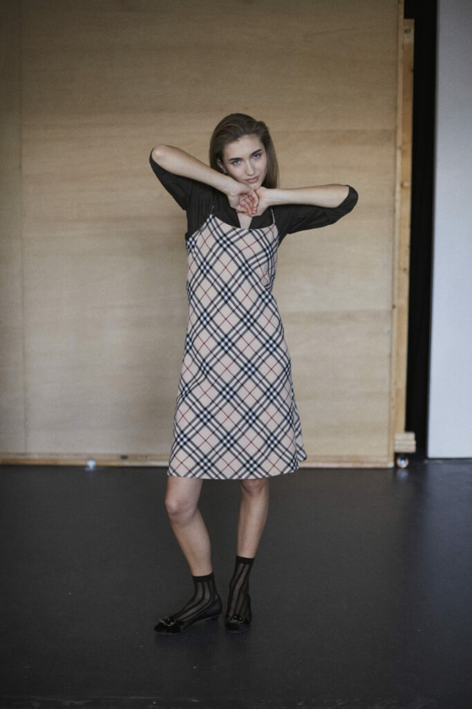 Weibliches Model in einem karierten Kleid vor einer Holwand im Fotostudio.