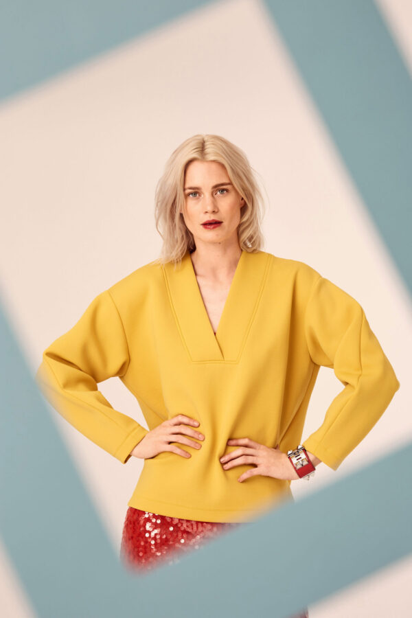 Blondes Model im Fotostudio schaut in die Kamera. Im vordergrund hält jemand einen papierrahmen ins Bild.