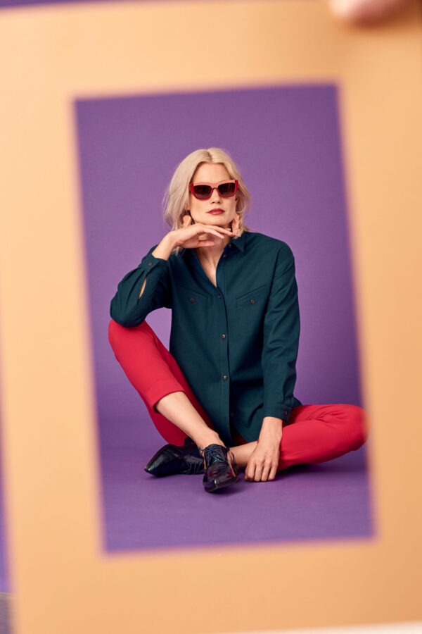 Weibliches blondes Model sitzt mit Sonnenbrille auf dem Boden eines Fotostudios.
