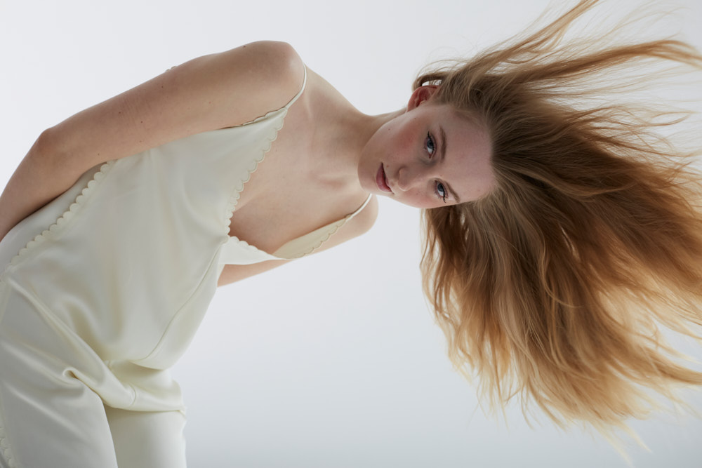 Weibliches blondes Model von unten fotografiert, mit den Haaren im Wind. 