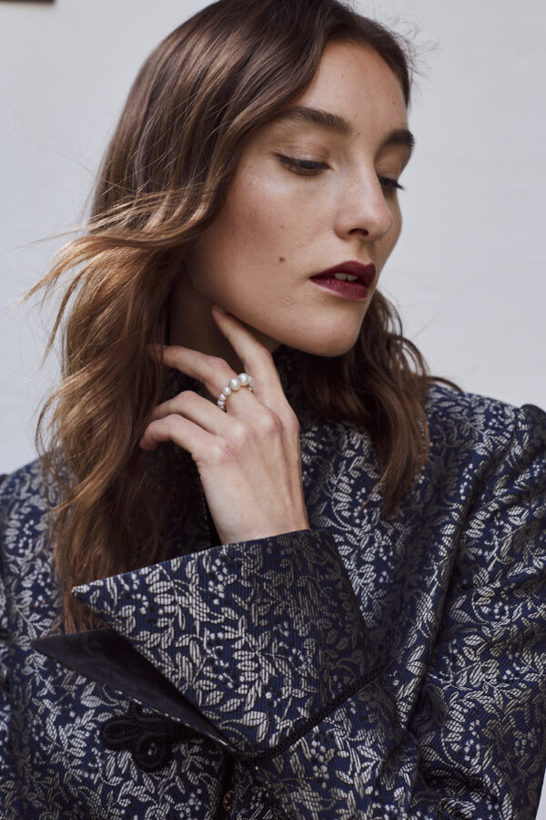 Braunhaariges weibliches Model, halt die Hand am Kinn, schaut nach unten. Sehr schick und weihnachtlich angezogen.