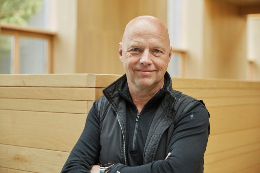 Ein mittelalter Mann mit Glatze steht mit Jacke vor einer holzvertäfelten Wand und schraut freundlich in die Kamera. Portrait für das Forbes Magazin von Fotografin Verena Vötter aus München.