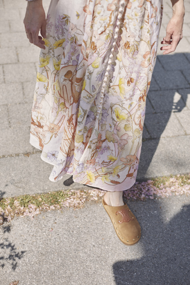 Ein sommerliches Kleid an einer Frau von oben fotografiert. Man sieht nur die Arme, Beine und die Strasse.