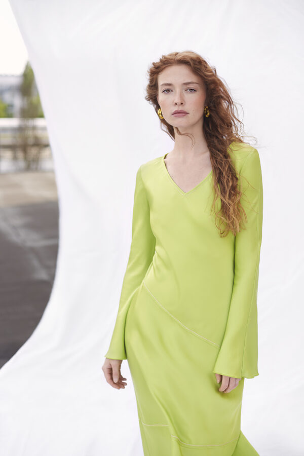 Weibliches Model in einem sehr eleganten Kleid mit langen Haaren vor einem weißen, fliessenden Stoffhintergrund auf einem Dach in München.