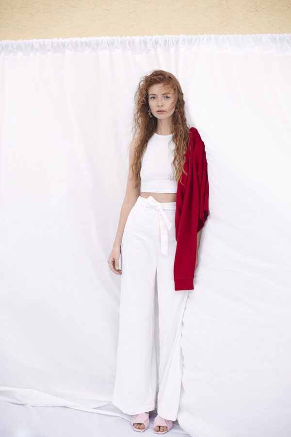 Weibliches schlankes Model steht vor einem weißen Stoffhintergrund. Sehr reduziert.