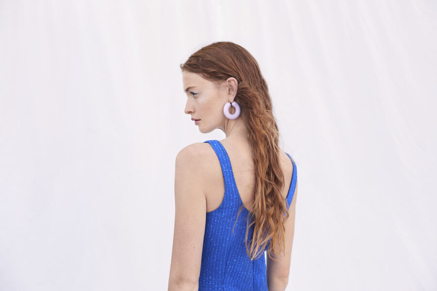 Weibliches Model von hinten fotografiert vor einem weißen Stoffhintergrund. Sommerlich, nüchtern.