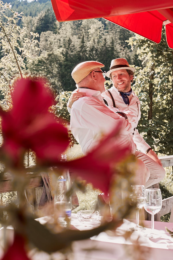 Ein schwules Paar auf einer Hochzeit, lacht sich an.