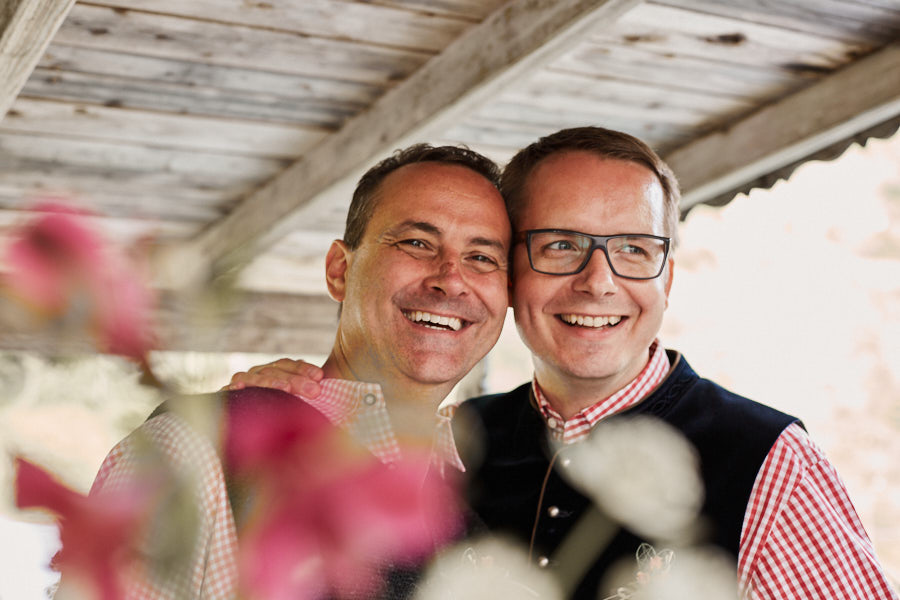 Schwules Paar in Tracht lacht in die Kamera.