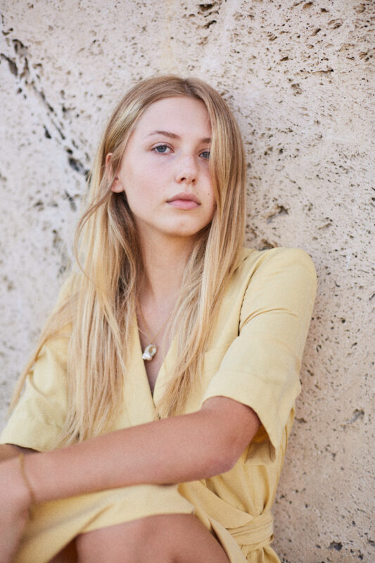 junge blonde Frau vor Naturwand.